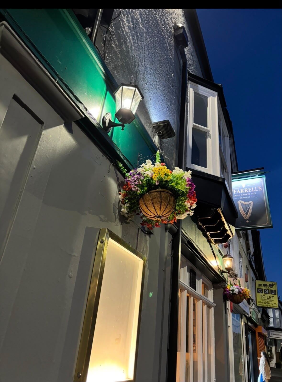 The O'Farrell's frontage on Brighton Road by day, black and gold signage with hanging flower baskets